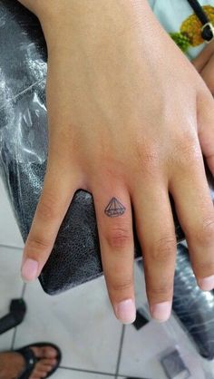 a person's hand with a small triangle tattoo on their left thumb and finger