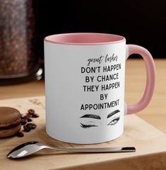 a pink and white coffee mug sitting on top of a wooden table next to a spoon