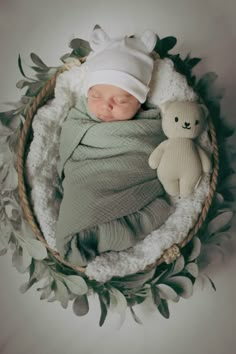 a newborn baby wrapped in a blanket with a teddy bear sitting next to it on a wreath