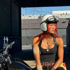 a woman with red hair wearing a helmet and sitting on a motorbike in front of a building