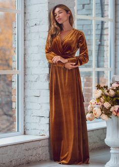 a woman standing in front of a window wearing a brown velvet dress with long sleeves