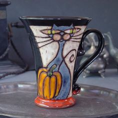 a black and white cat sitting on top of a coffee cup next to a silver tray