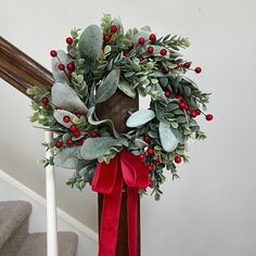 a christmas wreath on top of a banister with red ribbon and holly berries hanging from it