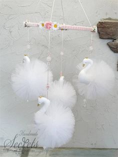 three white swan mobiles hanging from a string with pink flowers and pearls on them