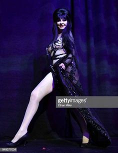 a woman with long black hair and high heels is posing on stage in front of a curtain