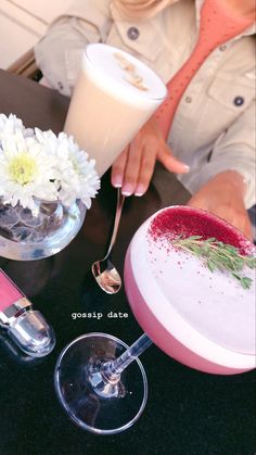 a woman sitting at a table with some drinks and flowers in vases on it