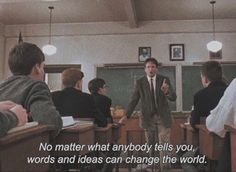 a man standing in front of a class room full of students with a quote written on the wall