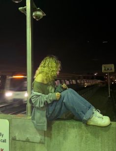 a woman sitting on the side of a wall next to a street light at night