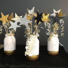 three mason jars filled with gold and silver stars on top of a black cloth covered table