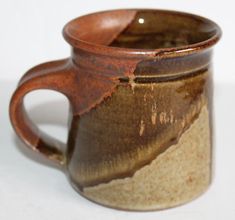 a close up of a coffee cup on a white surface with brown and tan glaze