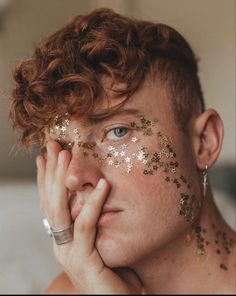 a woman with gold stars painted on her face and hands near her face, covering her eyes