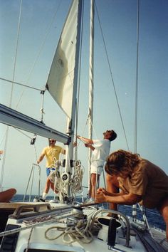 two men working on a sailboat while another man watches from the front deck in the background