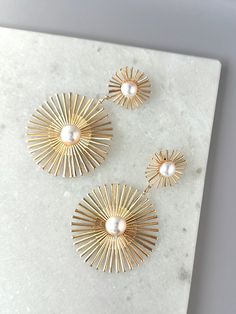 Elevate your style with our striking Sunburst Pearl Earrings! These statement drop earrings feature a lustrous pearl accent and are crafted in elegant gold, adding a touch of sophistication to any outfit. The abstract sunburst shape adds a unique touch to these must-have earrings. Make a bold fashion statement with our Sunburst Pearl Earrings! Elegant Starburst Earrings For Party, Elegant Sunburst Earrings As A Gift, Elegant Gold Starburst Jewelry, Gold Starburst Earrings For Party, Elegant Sun Design Drop Earrings, Elegant Gold Earrings With Sun Design, Gold Starburst Party Earrings, Elegant Gold Sunburst Jewelry, Elegant Sun Design Starburst Jewelry