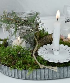 a candle is sitting on top of some moss and pineconis in a tin container