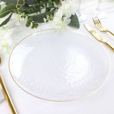 a white plate with gold rim sitting on top of a table next to silverware