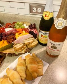 breads, fruit and wine are on the counter next to a plate with croissants