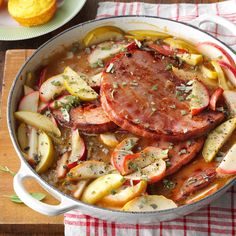 a pan filled with meat and vegetables on top of a wooden table next to bread