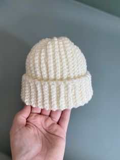 a hand holding up a white knitted hat