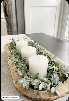 three candles sitting on top of a wooden tray filled with greenery and eucalyptus leaves