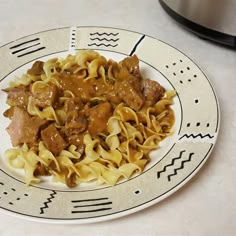 a white plate topped with pasta covered in meat and sauce next to an instant pot