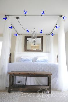 a bedroom with white bedding and curtains hanging from the ceiling, along with a wooden bench