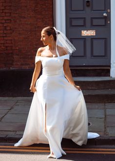 a woman in a white wedding dress is walking down the street with her veil over her head