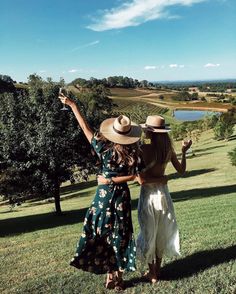 two women standing on top of a lush green field holding wine glasses in their hands