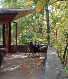 a person sitting on a bench in front of a covered porch with chairs and table