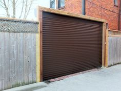 a closed garage door in front of a wooden fence and brick building on the street