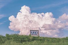 a large cloud is in the sky above a sign on top of a grassy hill