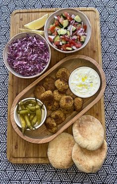 a wooden tray topped with different types of food next to bowls of vegetables and bread