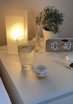 an alarm clock sitting on top of a white table next to a glass filled with water