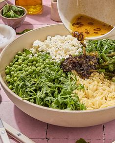 a bowl filled with pasta and greens being poured into it