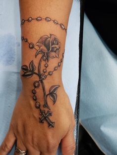 a person with a rosary and rose tattoo on their wrist