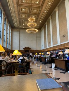 people sitting at tables in a large library with chandeliers hanging from the ceiling