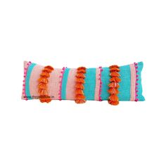 an orange and blue striped pillow with tassels on the edges, sitting on a white surface