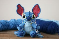 a crocheted blue and red stuffed animal next to skeins of yarn