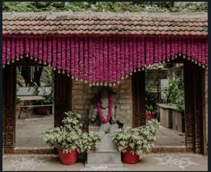 an outdoor shrine with pink flowers hanging from it's roof and decorations on the outside