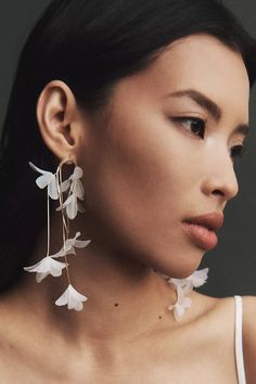 a woman wearing large white flowers on her ear and necklace, looking down at the camera