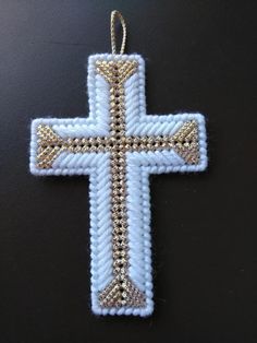 a white cross with gold trim on it is hanging from a string and sits on a black surface