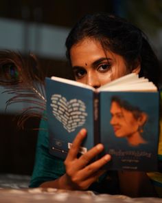 a woman is reading a book while laying on the floor with a peacock feather in front of her