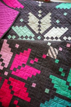 a black and pink quilt on top of a bed next to a red flower vase