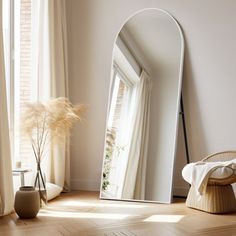 a large white mirror sitting on top of a wooden floor next to a chair and potted plant