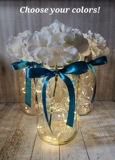 two mason jars with white flowers in them and blue ribbon around the top, on a wooden table