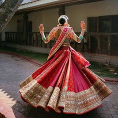 a woman in a red and gold lehenga is dancing on the street with her hands up