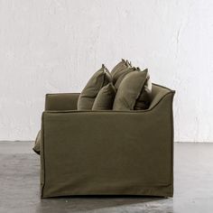 an olive green couch with four pillows on it and a white wall in the background