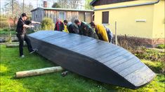 a group of people standing around a large boat in the middle of some grass and trees