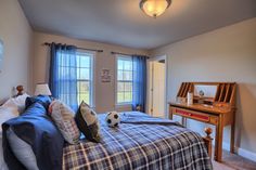 a bedroom with a soccer ball on the bed, and two windows in the room