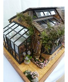 a miniature house made out of wood and glass with plants growing on the roof, in front of a white backdrop