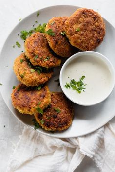 four crab cakes on a white plate with a small bowl of ranch dressing